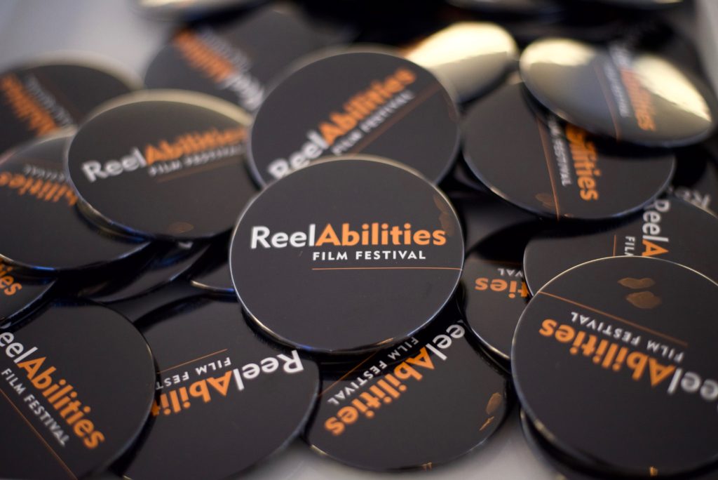 black buttons wit Reelabilities Film Festival logo on it in orange and white
