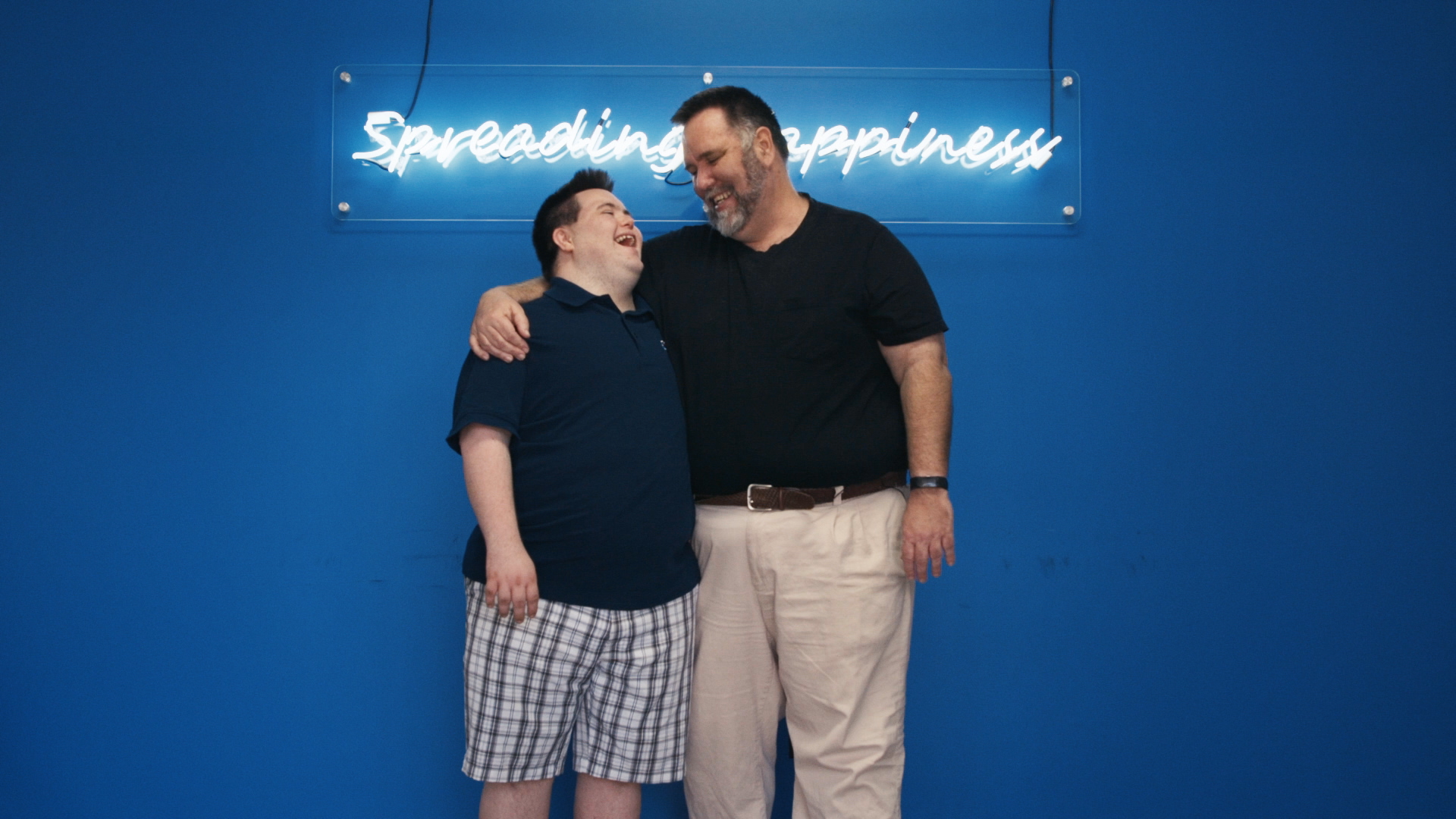 A father and son stand under a neon sign