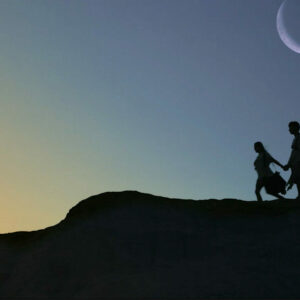 Shadows of two people appear on a mountain under a crescent moon and dusky sky.