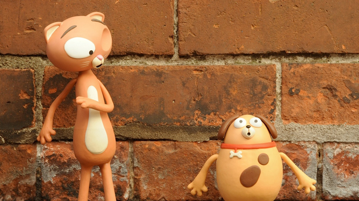 A toy cat and a toy dog stand against a brick wall