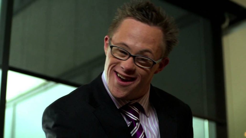 A man in a suit with glasses smiles brightly