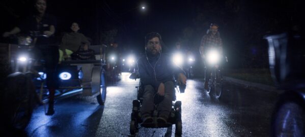 a man in a motorised wheelchair in the middle of the road, surrounded by bicycles and tricycles.