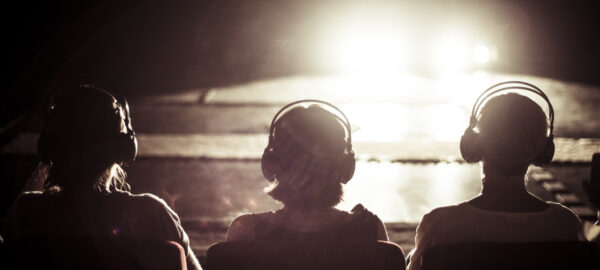 3 silhouettes of people seated with headphones on, looking at a glaring light in front of them
