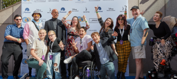 A group of people cheering in front of a film festival step and repeat banner