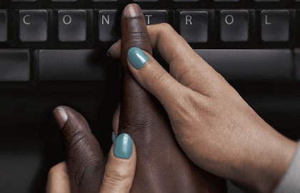 A white woman's hand holds a black man's hand over a computer keyboard.